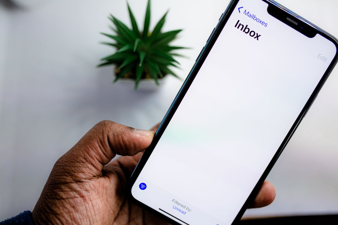 Un gros plan sur l'écran d'un smartphone affichant la boîte de réception des e-mails, tenu dans la main d'un adulte.